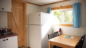 Una cocina compacta con paredes de madera, un refrigerador blanco, un lavamanos y una mesa de comedor con sillas.