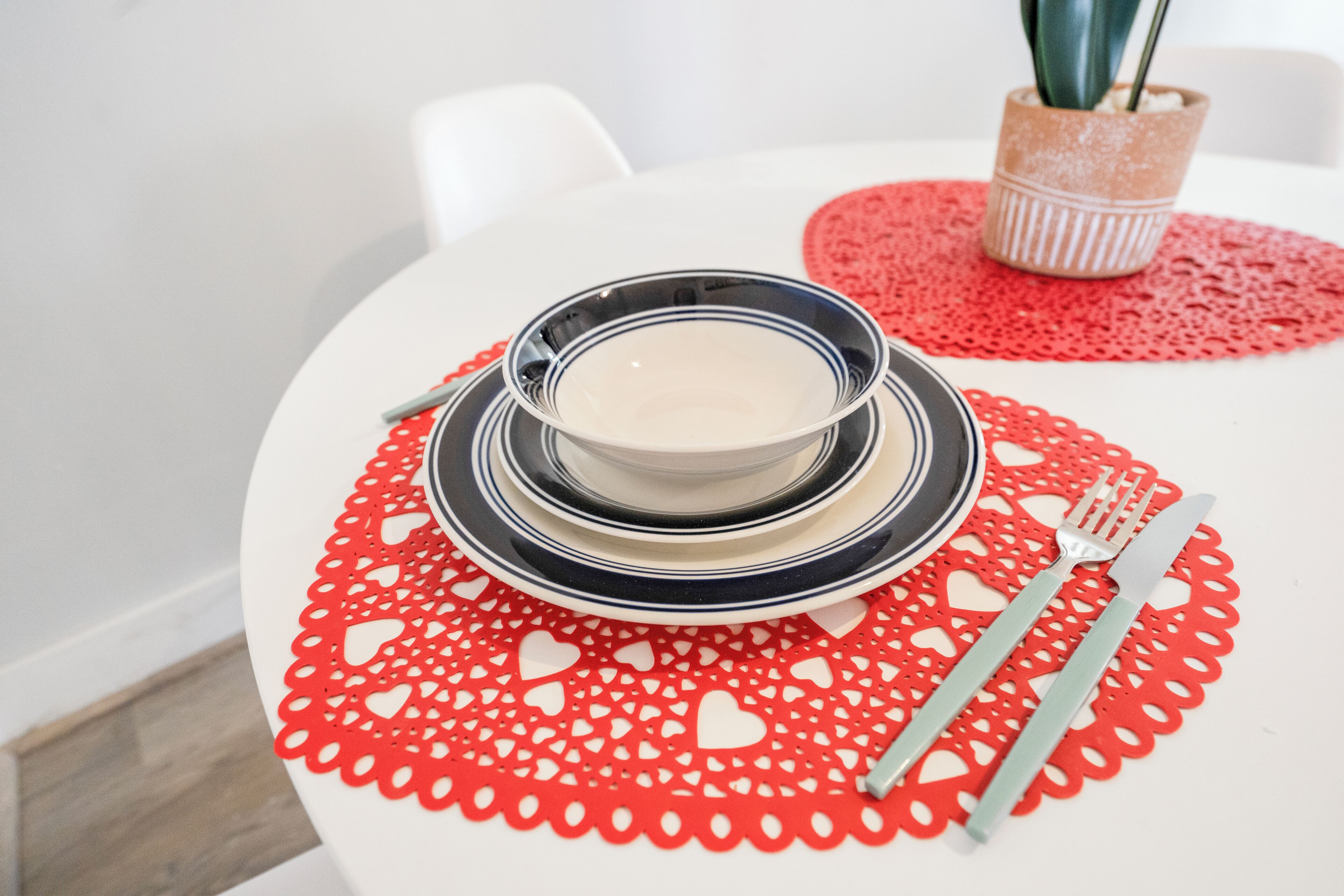 A dining table with a red heart-patterned table runner, a bowl of soup, and cutlery.