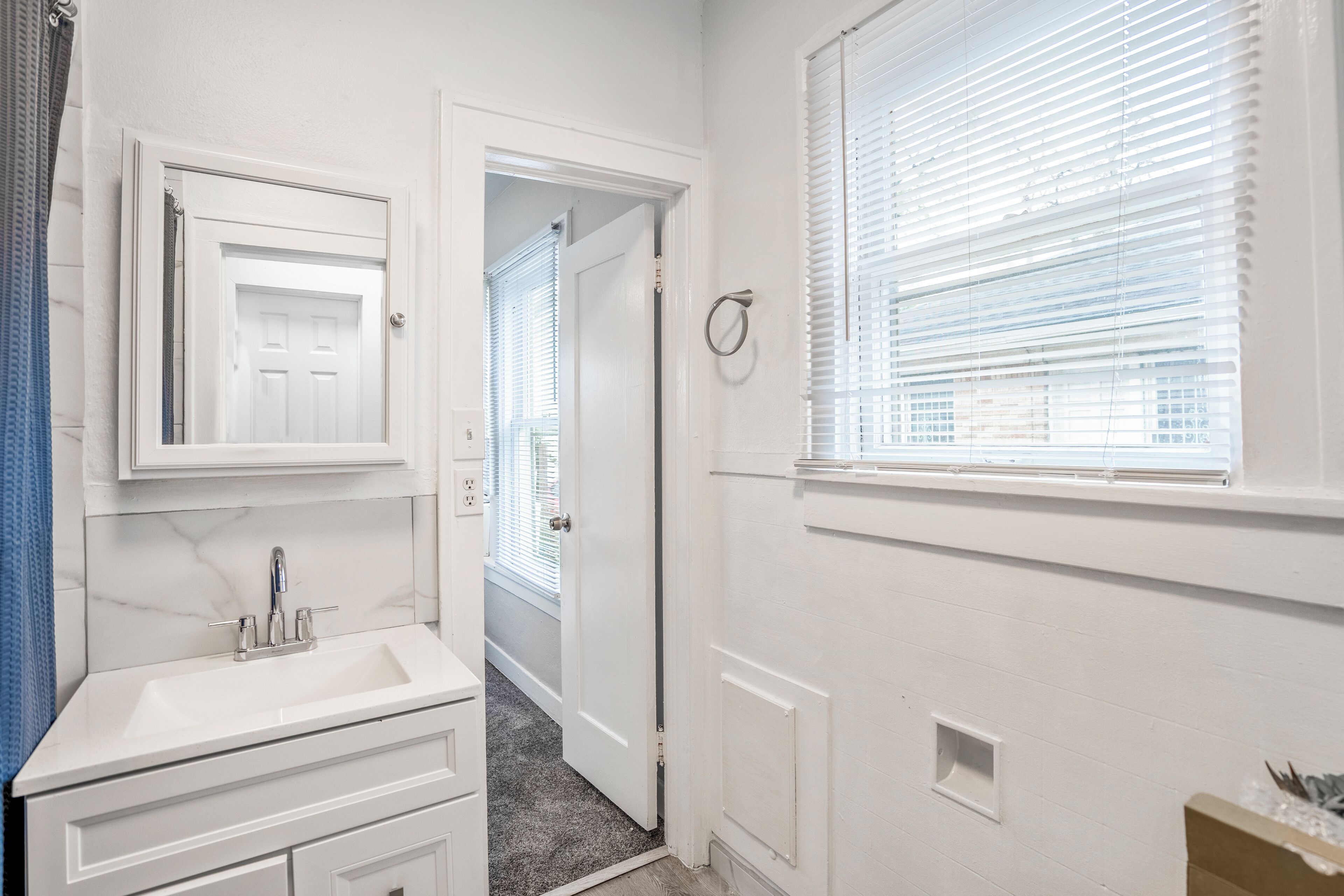 A bathroom with a white sink, mirror, and window with blinds.