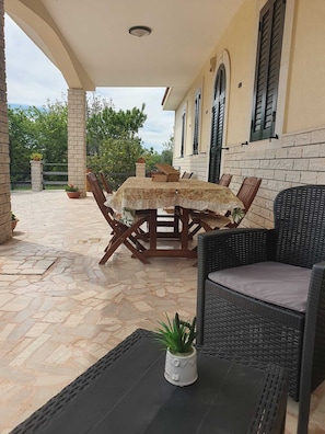An outdoor patio with a table and chairs, a potted plant, and a building with stone walls and shutters. - Villa Sideris, 3-bedroom villa  (Puglia)