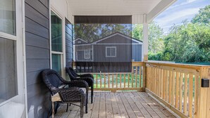 A covered porch with two wicker chairs, a wooden deck, and a view of a house in the background. - The Travelers Studio Columbus (Columbus)