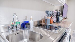 A stainless steel kitchen sink with a faucet, soap dispenser, and dish soap. There are utensils and a coffee maker on the countertop. - The Travelers Studio Columbus (Columbus)