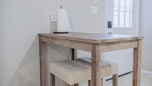 A wooden dining table with a bench, a wall-mounted wine glass and bottle art, and a door with a window. - The Travelers Studio Columbus (Columbus)