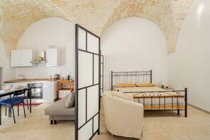 A compact room with a bed, a sofa, a dining area, and a kitchen.