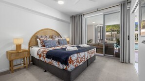 A bedroom with a bed, bedside tables, a ceiling fan, and a sliding glass door to a balcony.