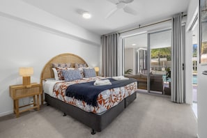 A bedroom with a bed, bedside tables, a ceiling fan, and a sliding glass door to a balcony.