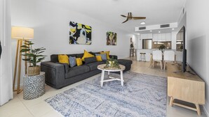 A modern living room with a grey sofa, yellow pillows, a round coffee table, and a dining area with a white table and chairs.