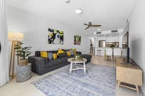 A modern living room with a grey sofa, yellow pillows, a round coffee table, and a dining area with a white table and chairs.