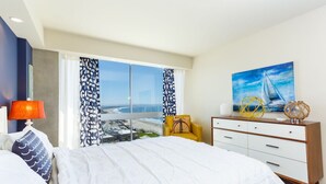A hotel room with a large bed, a nightstand with a lamp, a dresser, and a painting of a sailboat.