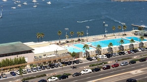 A coastal cityscape with a marina, a swimming pool, and a road with parked cars.