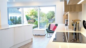 Une cuisine moderne avec des meubles blancs, un grand îlot central et une vue sur un jardin grâce à de grandes fenêtres.