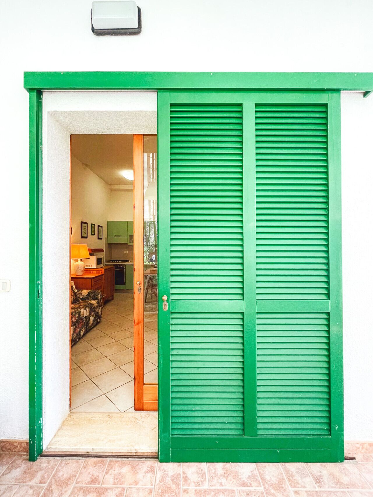 A green door leading into a room with a tiled floor and a kitchen visible through the doorway.