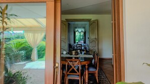 A dining area with a table and chairs, a window with curtains, and a view of greenery outside. - Villa Magnolia - Pula (Pula)