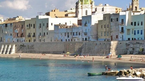 A coastal town with a prominent building featuring a dome and bell tower, a sandy beach, and boats in the water. - Romano Apartment - Trapani (Trapani)