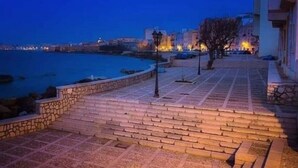 A paved waterfront promenade with stone steps leading to a body of water, surrounded by buildings with warm lighting. - Romano Apartment - Trapani (Trapani)