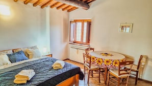 Un dormitorio con cama, una mesa con sillas, una ventana y un radiador.