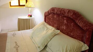 Ein Schlafzimmer mit Bett, Kissen, einem Nachttisch, einer Lampe und einem Fenster.