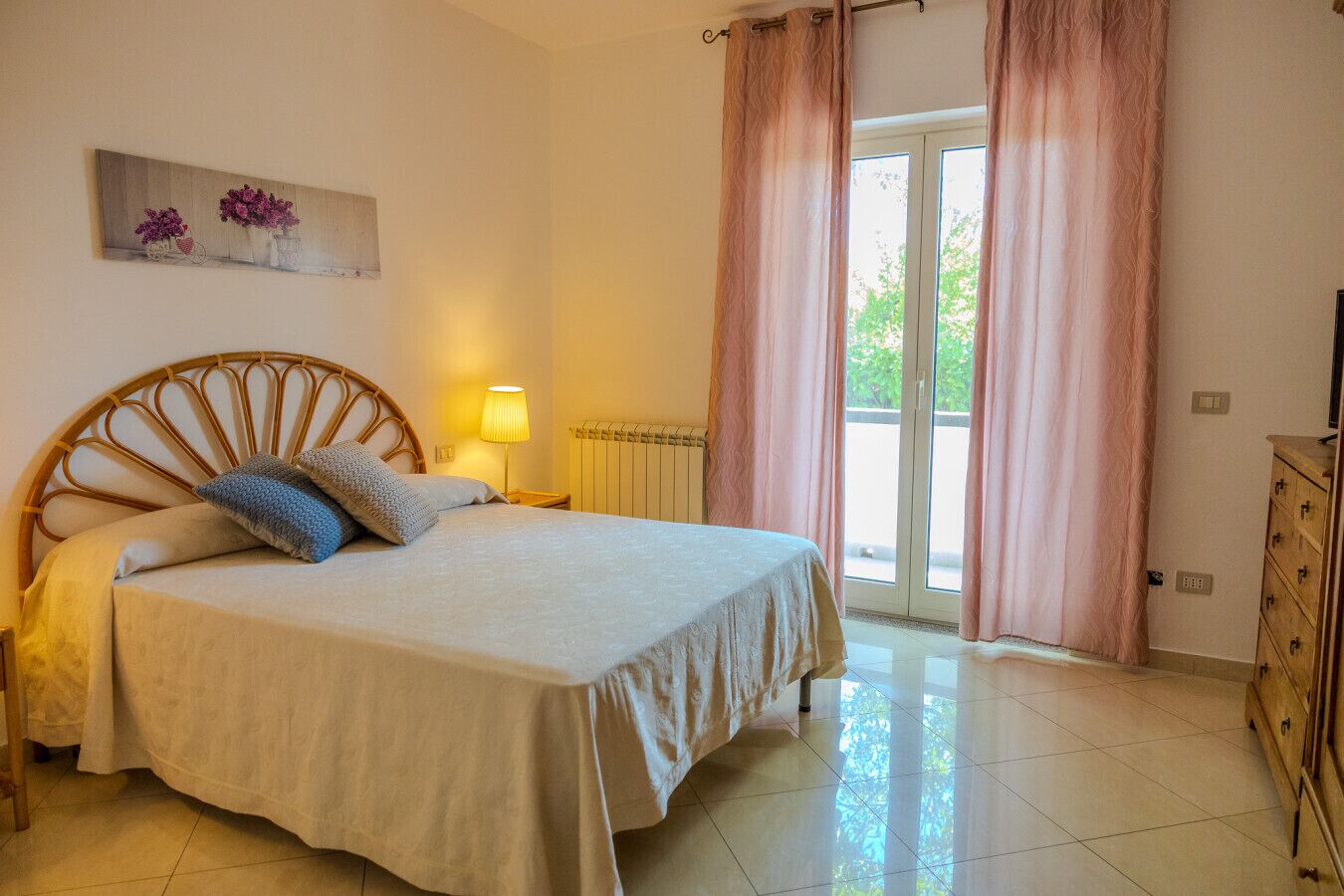 Un dormitorio con cama, mesita de noche, lámpara, cómoda y ventana con cortinas.