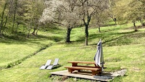 Un espace pique-nique équipé d’une table et de bancs en bois, entouré d’arbres et d’herbe.