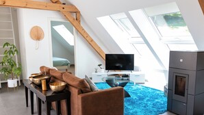 Un loft moderne avec un plafond en pente, un canapé marron, une table basse en verre, un téléviseur à écran plat, une cheminée et un tapis bleu.