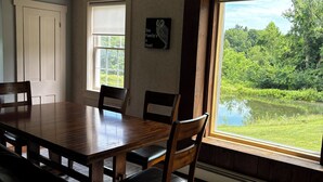A dining area with a wooden table, chairs, a rug, and a view of a pond through a large window. - Spacious 5-bedroom house in nice Winfield with WiFi, Pool and Hot tub (Winfield)