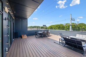 A rooftop deck with outdoor seating, a trash bin, and a view of the city skyline.