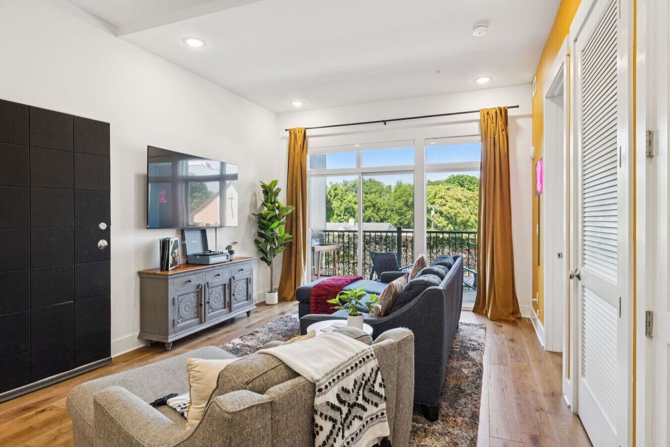A modern living room with a sofa set, a flat-screen TV, and a large window with curtains.