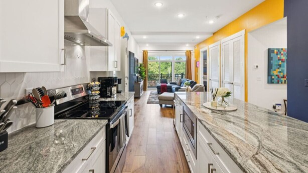 A modern kitchen with granite countertops, stainless steel appliances, and a view to a balcony.