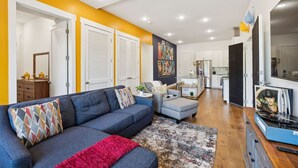 A modern living room with a blue sofa, a red throw blanket, and a colorful rug.