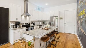 A modern kitchen with white cabinets, stainless steel appliances, a large island with bar stools, and a cityscape mural on the wall.