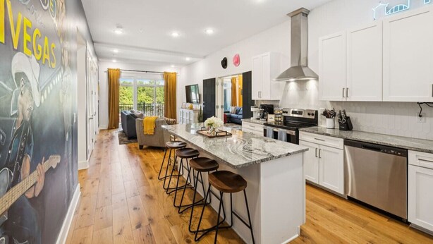 A modern kitchen with a central island, bar stools, and a view to a living area.