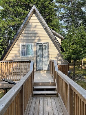 Une cabane en bois avec une porte d’entrée, une fenêtre et une terrasse en bois menant à l’entrée.