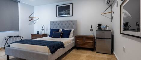 A modern bedroom with a bed, bedside tables, a dresser, a refrigerator, and a framed picture on the wall.