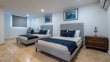 A modern bedroom with two beds, a large window with blinds, and a nightstand with a lamp.