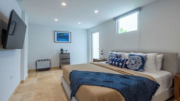 A bedroom with a bed, a TV mounted on the wall, a window, and a small table with a lamp.