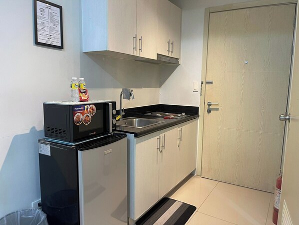 A compact kitchenette with a microwave, sink, and cabinets. There is a framed welcome sign on the wall. - Jazz residences Makati city by darpm (Makati)
