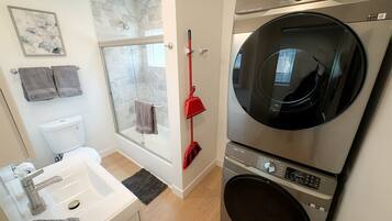 A compact bathroom with a shower, a sink, and a stacked washer and dryer.