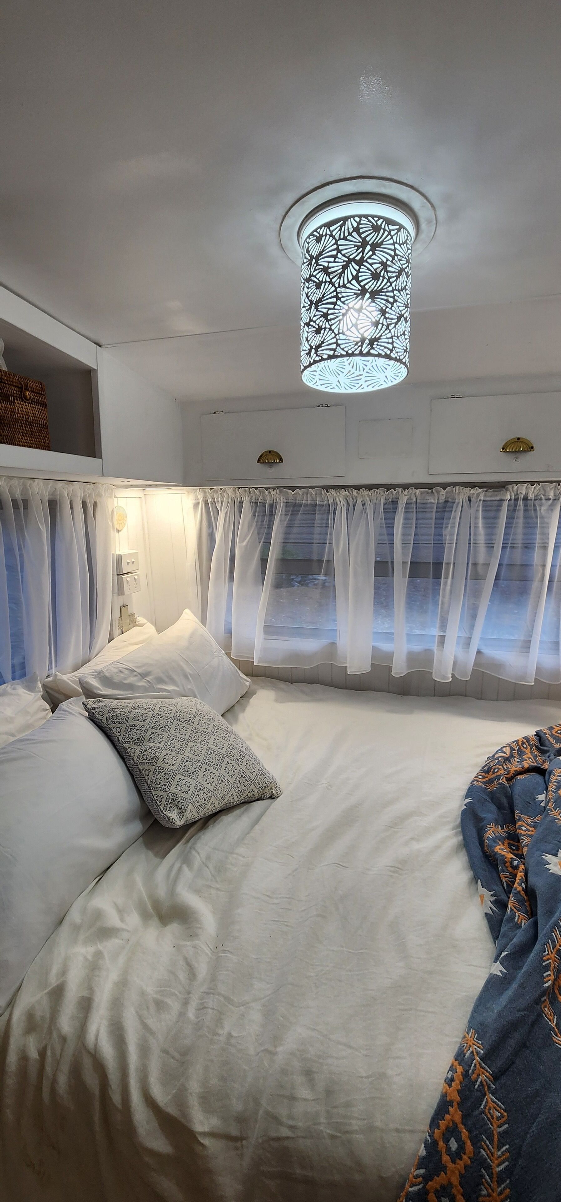 A neatly made bed with white linens and patterned pillows, a hanging light fixture, and sheer curtains.