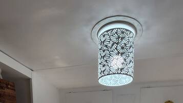 A neatly made bed with white linens and patterned pillows, a hanging light fixture, and sheer curtains.