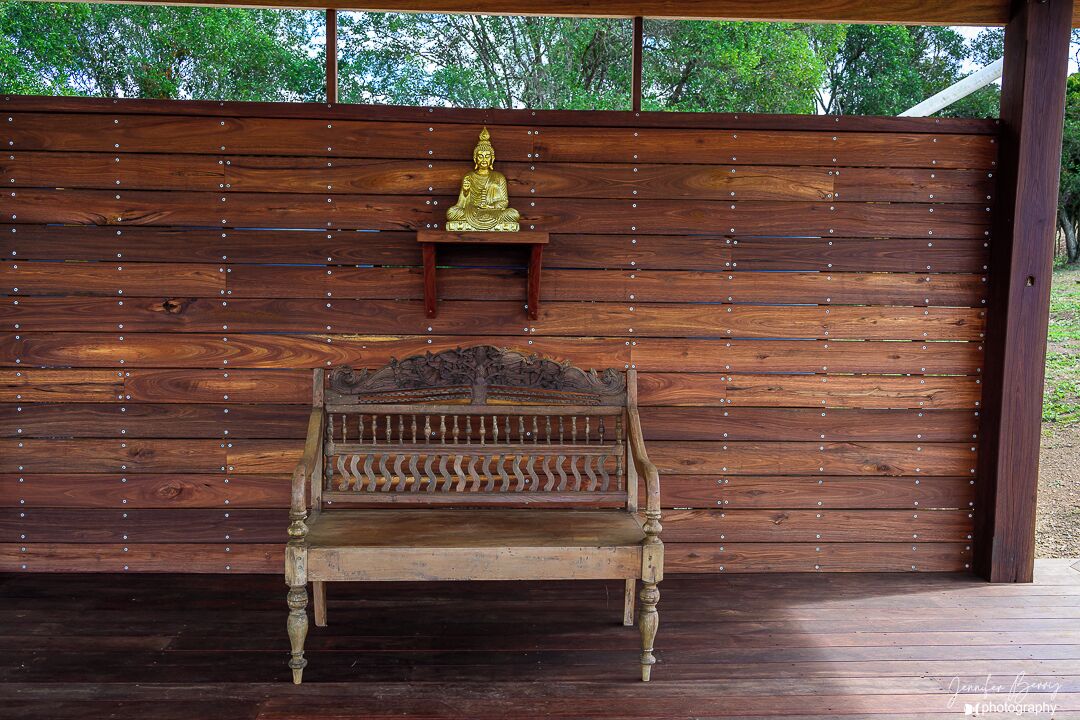 Un banc en bois doté d’un dossier décoratif et d’une petite étagère sur laquelle repose une statuette dorée.