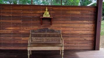 Un banc en bois doté d’un dossier décoratif et d’une petite étagère sur laquelle repose une statuette dorée.