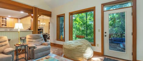 A living room with a bean bag, two armchairs, a coffee table, and a view of the outdoors through large windows.