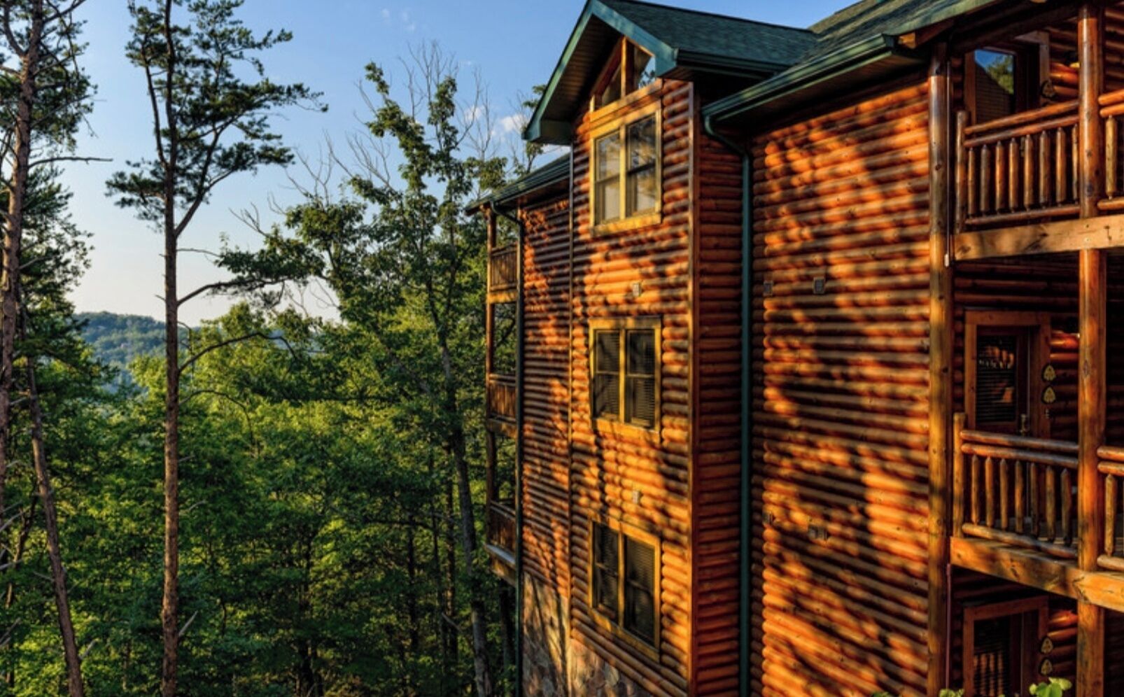 Une cabane en rondins dotée de nombreuses fenêtres et d’un balcon, entourée d’une forêt dense.