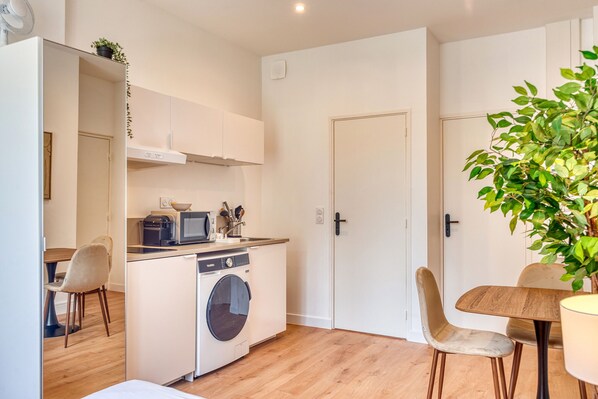 A compact kitchen with a washing machine, microwave, and a dining area with chairs and a table.