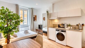 Een compacte hotelkamer met een bed, een klein tafeltje, een wasmachine, een magnetron en een wastafel.