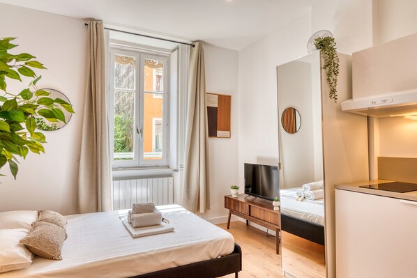 Habitación de hotel moderna con una cama grande, un televisor, un escritorio pequeño y vistas al exterior.