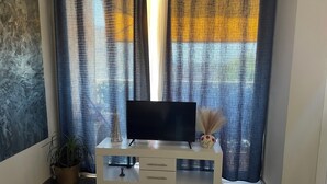 Una sala de estar con un mueble blanco para el televisor, una planta en maceta y un jarrón con plantas secas.