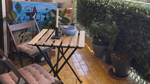 Un balcón con una mesa de madera, sillas y plantas en macetas.