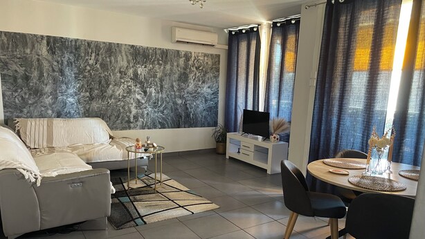 Una sala de estar moderna con sofá, mesa de centro, mueble para televisión y comedor con sillas y una mesa.