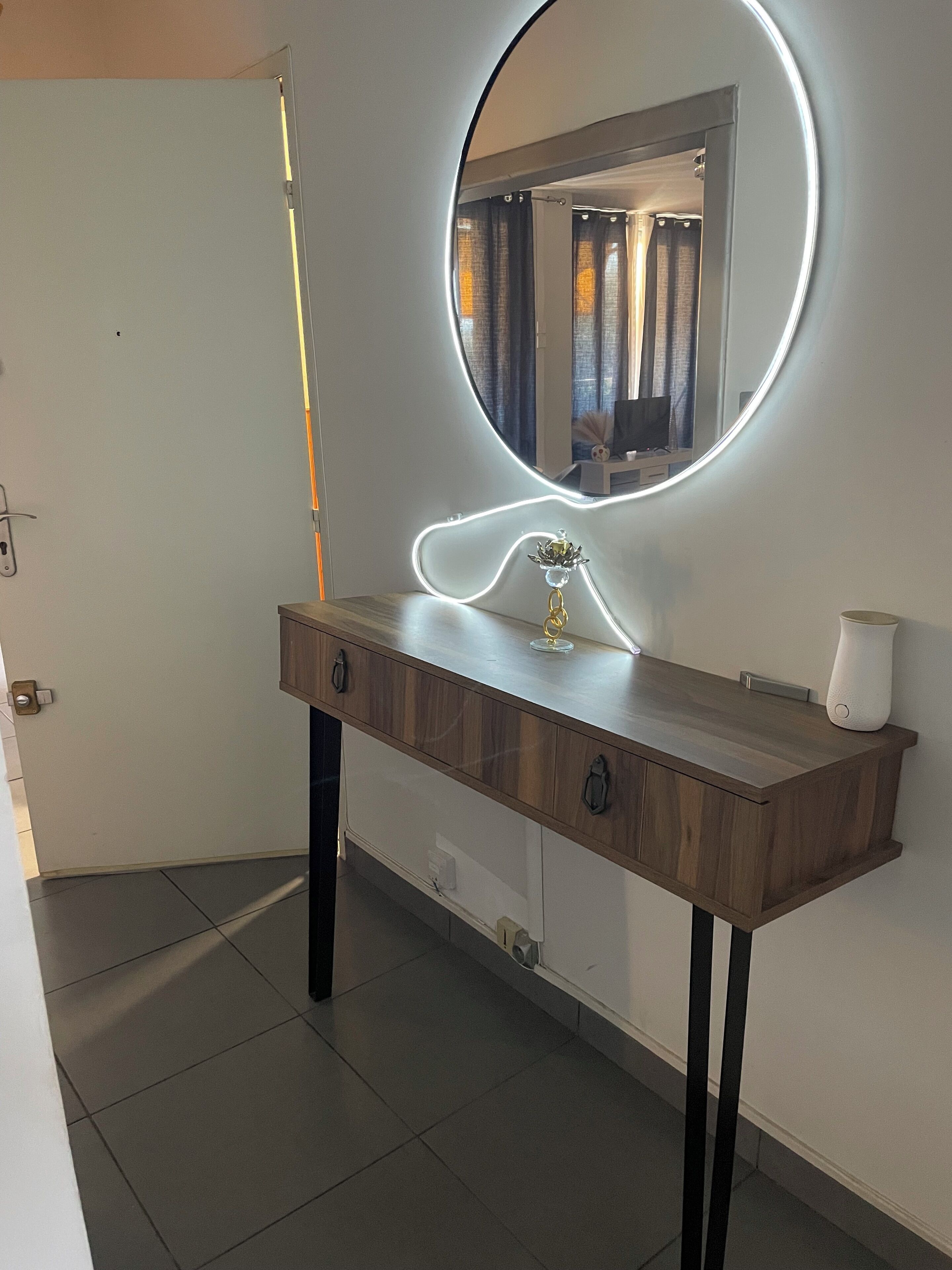 A bathroom vanity with a round mirror, a lighted vanity, and a white soap dispenser.
